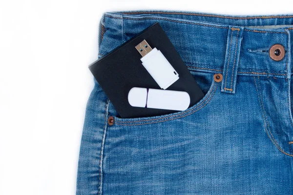 External hard drive and two flash drives are lying in a side pocket of blue jeans.