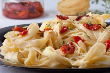Güneşte kurutulmuş domates ve biberiye ile Fettuccine makarna siyah bir tabak üzerinde yatıyor. Yakın çekim.