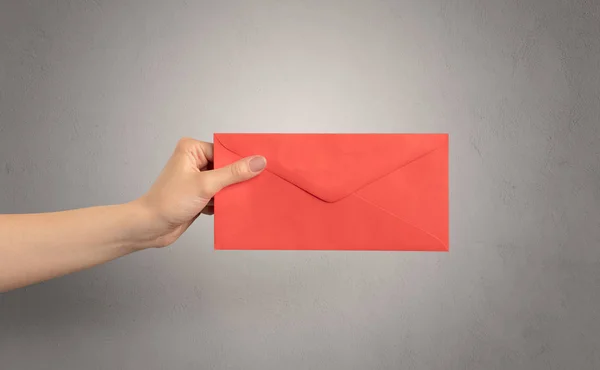 Hand holding envelope with empty wall background