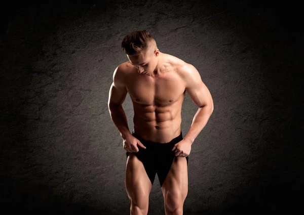 A handsome fitness guy lifting weight and showing his strong muscles in front of a black urban concrete wall concept — Stock Image Handsome Fitness Guy Lifting Weight Showing His Strong Muscles Front Stock Picture