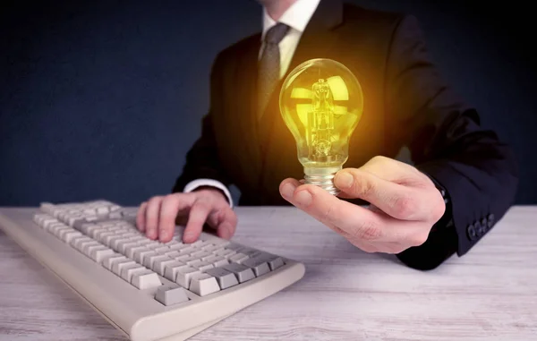 Man in suit holding a glowing yellow light bulb — Stock Photo, Image