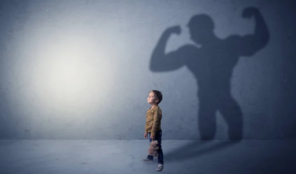 Muscleman shadow behind waggish little boy — Stock Photo, Image