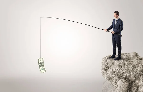 Businessman fishing dollar from a rock — Stock Photo, Image