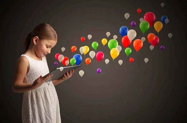 Menina segurando comprimido com balões coloridos ao redor — Fotografia de Stock