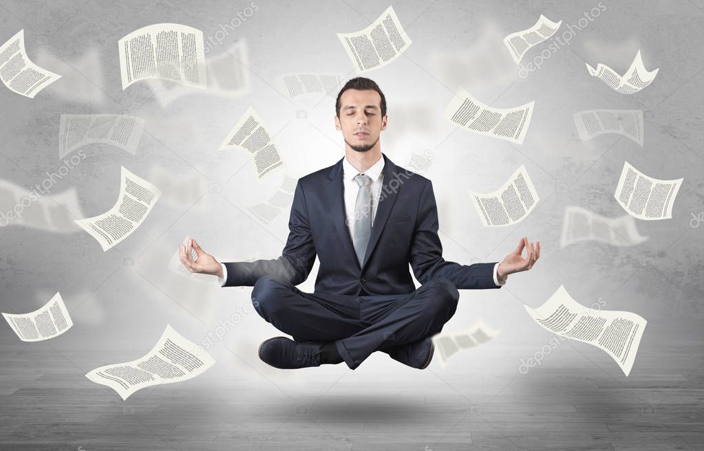 Businessman meditating with flying paper concept