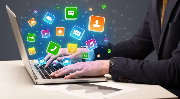 Hand using laptop with application icons flying around — Stock Photo, Image