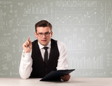Beyaz grafik ve hesaplamalar arkasında bir masada oturan genç yakışıklı işadamı 