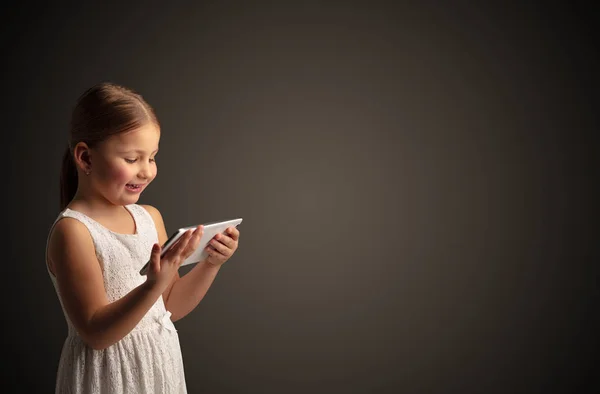 Nettes kleines Mädchen mit Tablet mit dunklem Hintergrund — Stockfoto