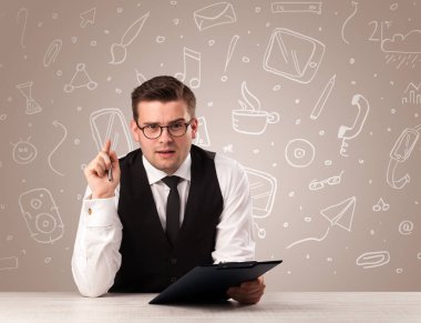 Onun arkasında beyaz karışık medya simgeleri ile bir masada oturan genç yakışıklı işadamı