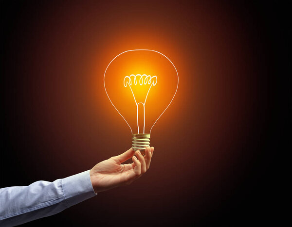 рука держа лампочку на темном фоне