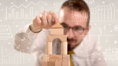 Genç yakışıklı işadamı Ahşap yapı taşları ile beyaz hesaplamalar kullanarak etrafında karalanmış