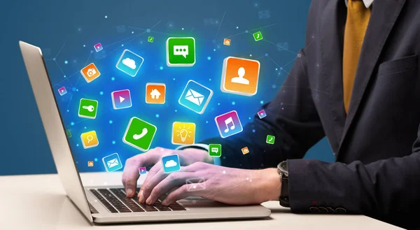 Hand using laptop with application icons flying around — Stock Photo, Image