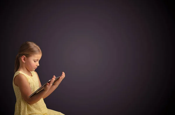 Petite fille mignonne utilisant une tablette avec un fond sombre — Photo
