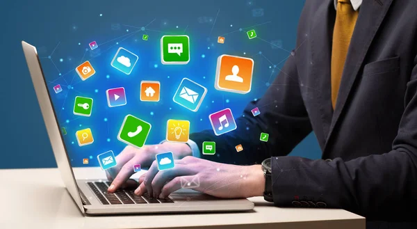 Hand using laptop with application icons flying around — Stock Photo, Image