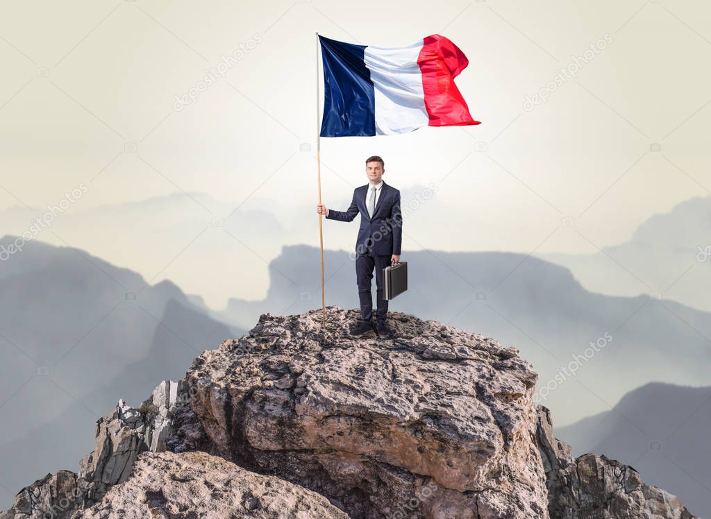 Businessman on the top of a rock holding flag