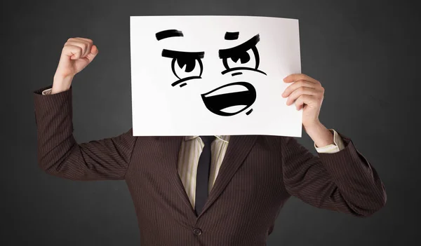Persona sosteniendo un papel con divertido emoticono delante de su cara — Foto de Stock