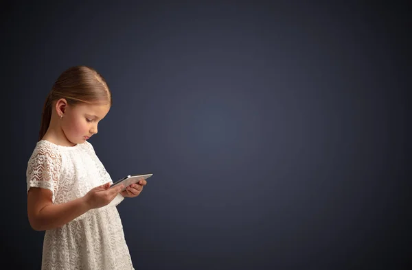 Nettes kleines Mädchen mit Tablet mit dunklem Hintergrund — Stockfoto