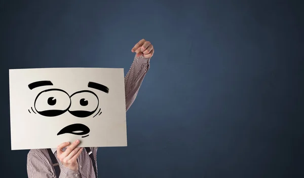 Persona che tiene un foglio con emoticon divertente davanti al suo viso — Foto Stock