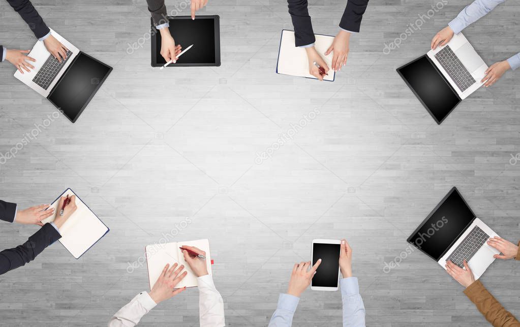 Group of people with devices in hands having desk discussion and making reports together on laptop, tablet, notebook