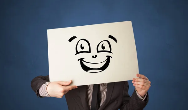 Person holding a paper in front of his face with doodle emoticon — Stock Photo, Image