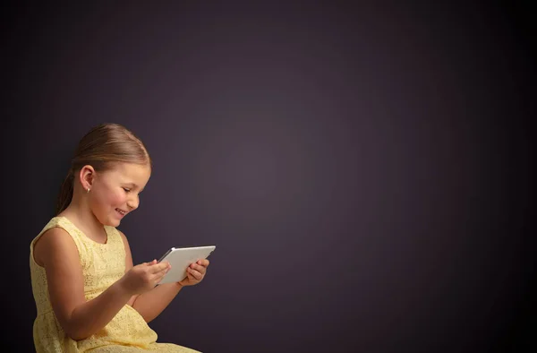 Nettes kleines Mädchen mit Tablet mit dunklem Hintergrund — Stockfoto