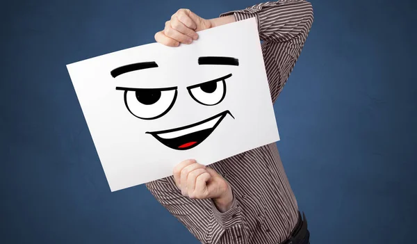 Pessoa segurando um papel na frente de seu rosto com doodle emoticon — Fotografia de Stock