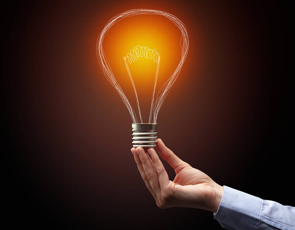 рука держа лампочку на темном фоне