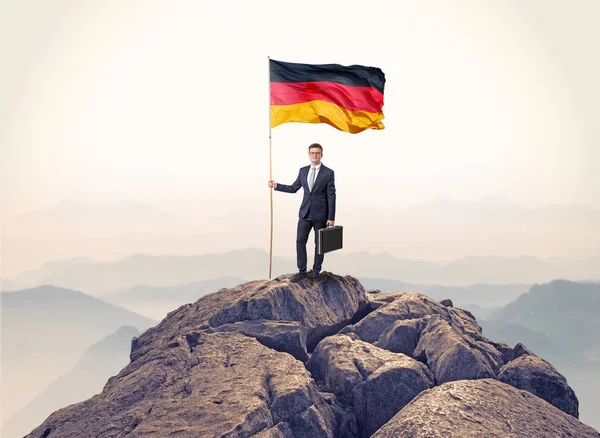 Affärsman på toppen av en klippa som håller flaggan — Stockfoto