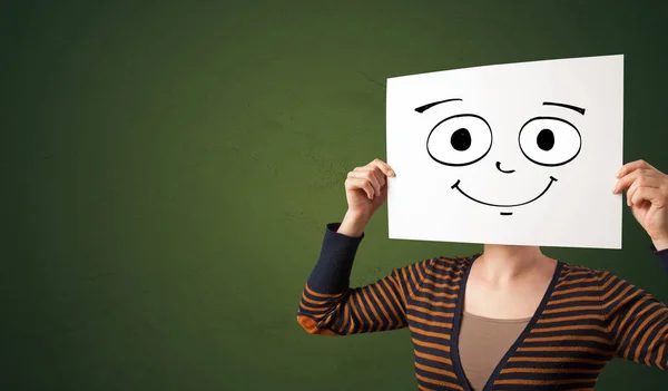 Estudante segurando um papel com emoticon rindo na frente de seu rosto — Fotografia de Stock