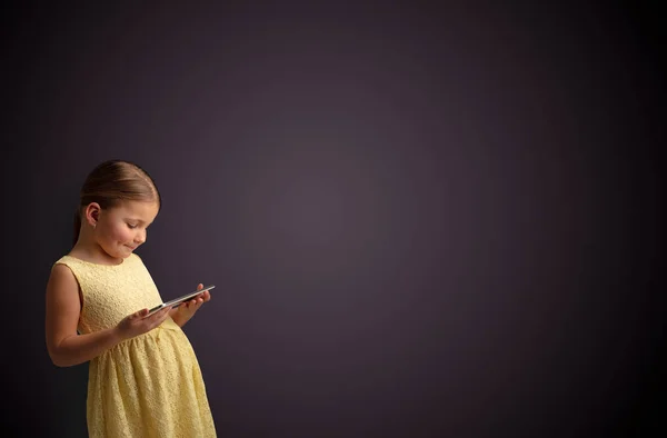 Nettes kleines Mädchen mit Tablet mit dunklem Hintergrund — Stockfoto