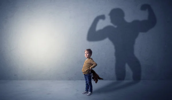 Muscleman shadow behind waggish little boy — Stock Photo, Image