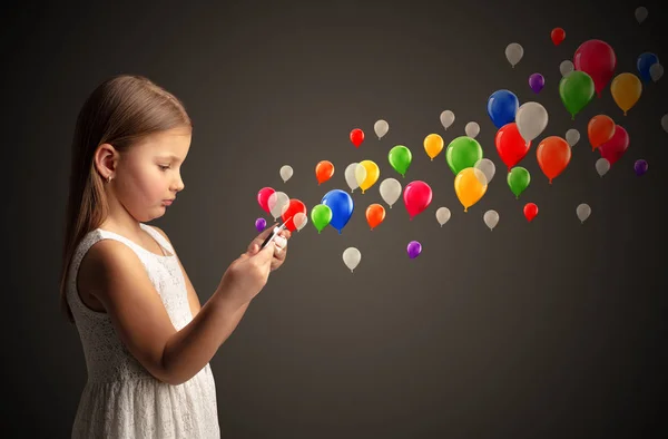 Menina segurando comprimido com balões coloridos ao redor — Fotografia de Stock