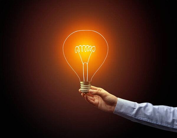 рука держа лампочку на темном фоне