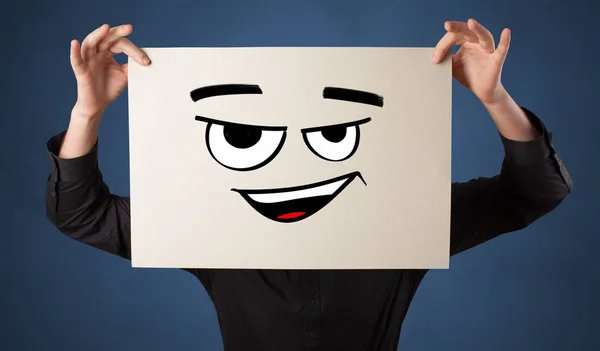 Pessoa segurando um papel na frente de seu rosto com doodle emoticon — Fotografia de Stock