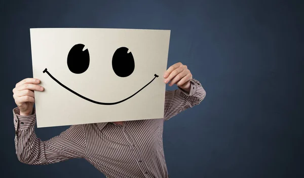 Person holding a paper with funny emoticon in front of her face — Stock Photo, Image