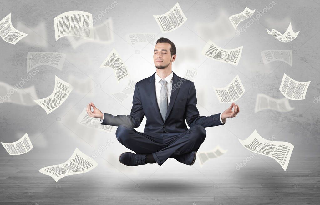 Businessman meditating with flying paper concept