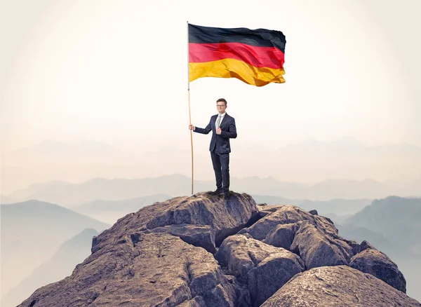 Businessman on the top of a rock holding flag