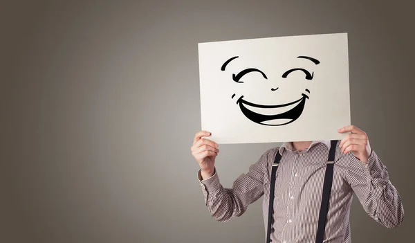 Persona che tiene un foglio davanti alla faccia con emoticon scarabocchiare — Foto Stock