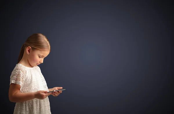 Nettes kleines Mädchen mit Tablet mit dunklem Hintergrund — Stockfoto