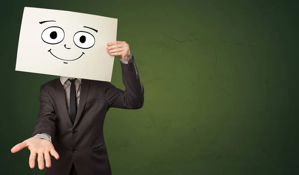 Estudante segurando um papel com emoticon rindo na frente de seu rosto — Fotografia de Stock