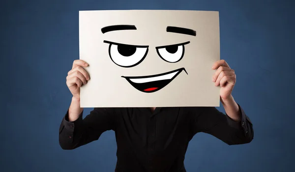 Pessoa segurando um papel na frente de seu rosto com doodle emoticon — Fotografia de Stock