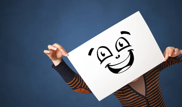 Person hält ein Papier vor sein Gesicht mit einem Doodle-Emoticon — Stockfoto
