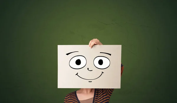 Estudante segurando um papel com emoticon rindo na frente de seu rosto — Fotografia de Stock