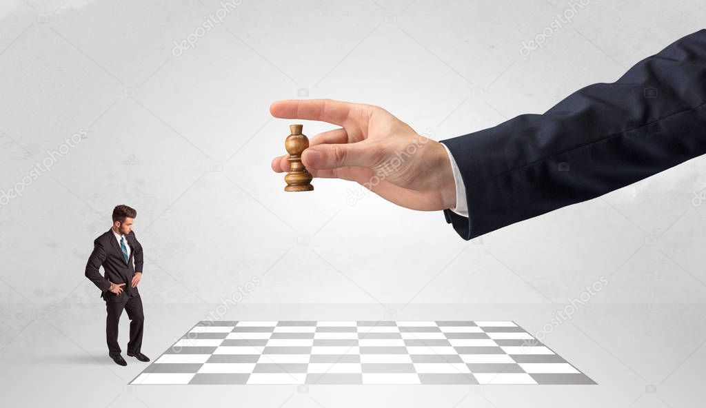 Little businessman playing chess with a big hand concept