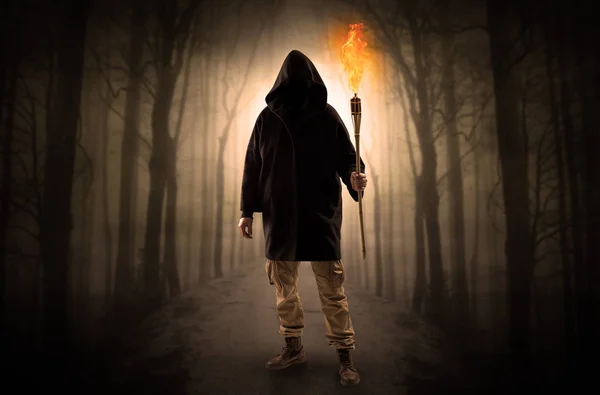 Человек, выходящий из тёмного леса с горящим пламенем в руке — стоковое фото