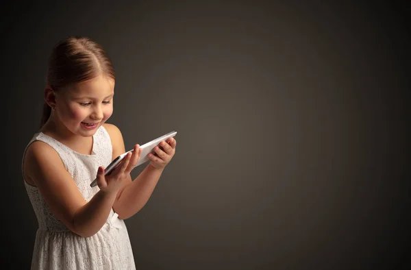 Nettes kleines Mädchen mit Tablet mit dunklem Hintergrund — Stockfoto