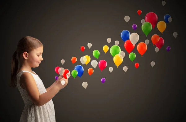 Menina segurando comprimido com balões coloridos ao redor — Fotografia de Stock