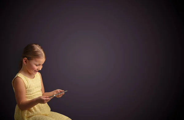 Nettes kleines Mädchen mit Tablet mit dunklem Hintergrund — Stockfoto