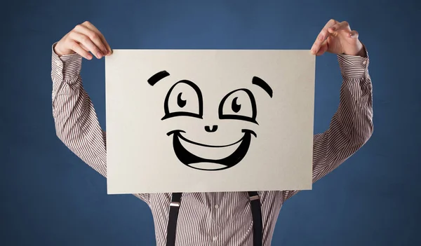 Person hält ein Papier vor sein Gesicht mit einem Doodle-Emoticon — Stockfoto