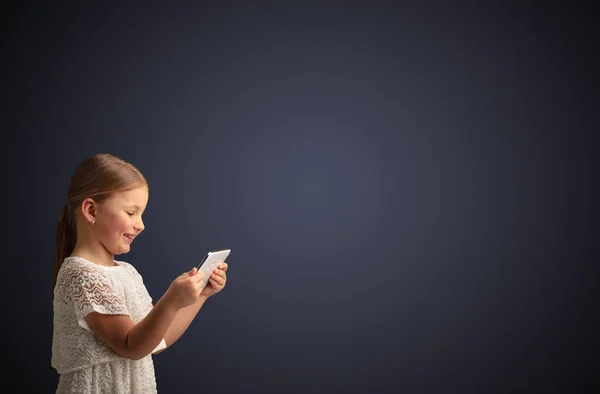 Nettes kleines Mädchen mit Tablet mit dunklem Hintergrund — Stockfoto